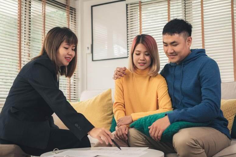 insurance-consultation-couple-financial-adviser A financial adviser meeting with a young couple at home, discussing insurance or investment documents in a relaxed setting